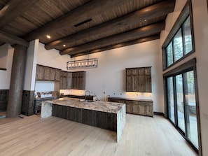 A spacious kitchen with a large island, wooden cabinets, and a view through large windows.