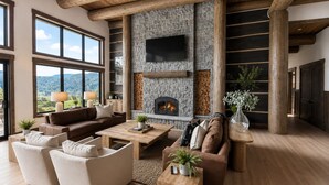 Un salón amplio con chimenea de piedra, ventanas grandes y un techo alto con vigas a la vista.