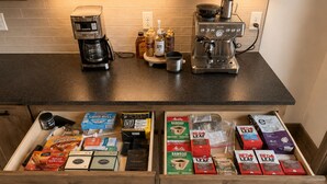 Una cocina con dos cafeteras, una jarra de café y un cajón con diferentes cápsulas y recipientes de café.