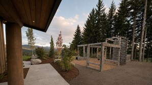 Una pérgola de madera en un jardín ajardinado, con vista a un bosque y montañas distantes.