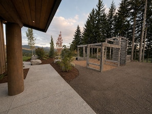 A wooden pergola structure in a landscaped garden with a view of a forest and distant mountains.
