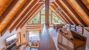 Un acogedor cuarto ático con techo de madera, chimenea, sofá y escritorio con libros.