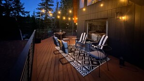 Una terraza de madera con mobiliario exterior y luces colgantes.