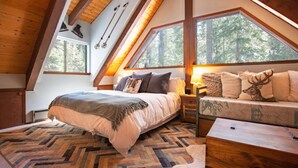 Un dormitorio acogedor en el ático con una cama grande, un sofá con cojines decorativos y vistas al bosque a través de tragaluces.