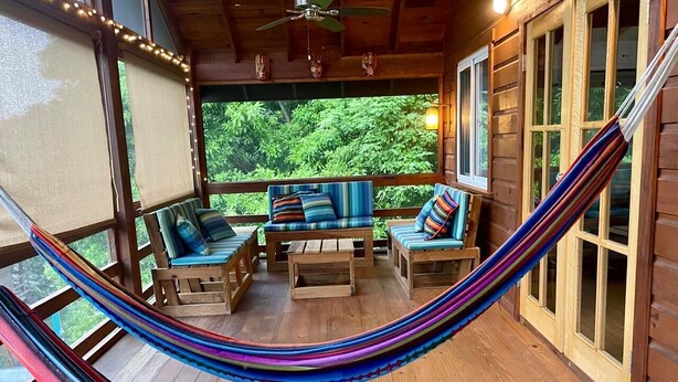 Un hamac installé sur une terrasse en bois, avec des meubles d’extérieur et de grandes fenêtres.