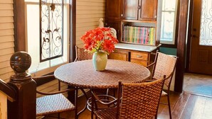 A dining area with a round table and wicker chairs, a vase with red flowers, and a bookshelf with books. - The Historic Myrna Loy House, Downtown Hot Springs (Hot Springs)
