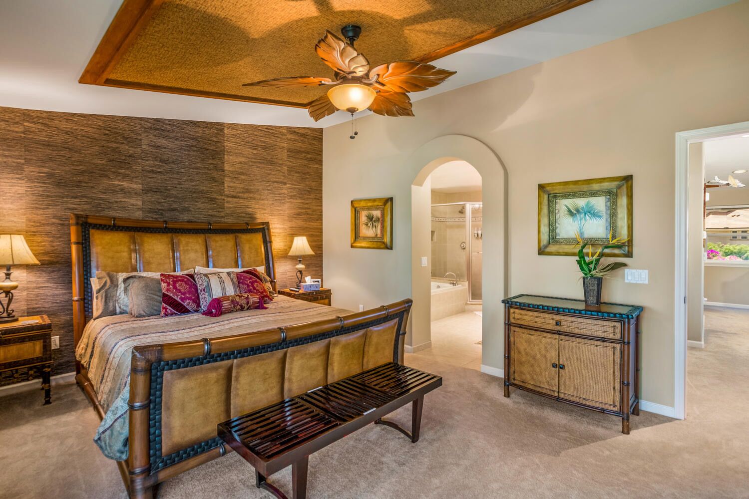 A bedroom with a large bed, a wooden bench, a ceiling fan, and a console table with a plant.