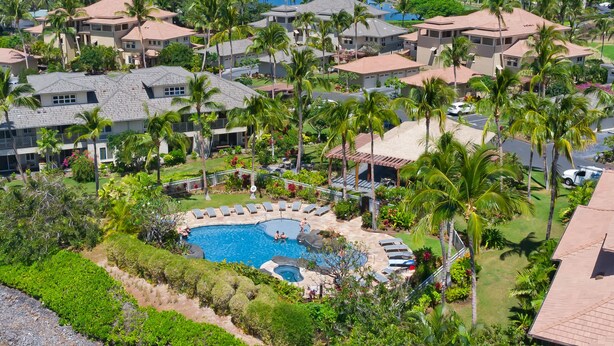 Ein Resort mit einem zentral gelegenen Schwimmbad, umgeben von Liegestühlen, Palmen und einem Golfplatz im Hintergrund.