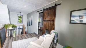 A cozy room with a large sliding barn door, a comfortable chair, a small table with a plant, and a framed picture on the wall. - Cozy Lakefront! Lac La Nonne, Alberta (Barrhead County No.11)