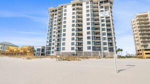 Un hôtel de grande hauteur doté de nombreux balcons, situé sur une plage dont le rivage est sablonneux et qui offre une vue sur un ciel bleu dégagé.