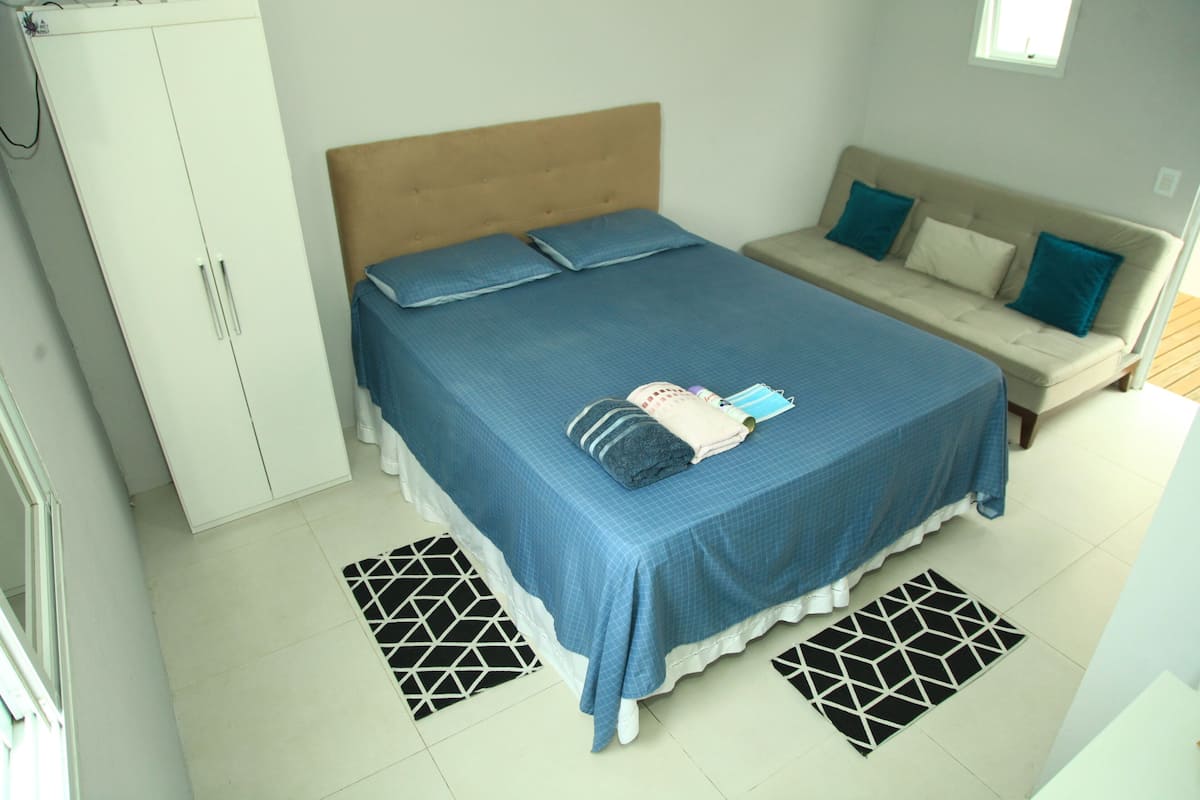 A bedroom with a bed, a wardrobe, a sofa, and patterned rugs.
