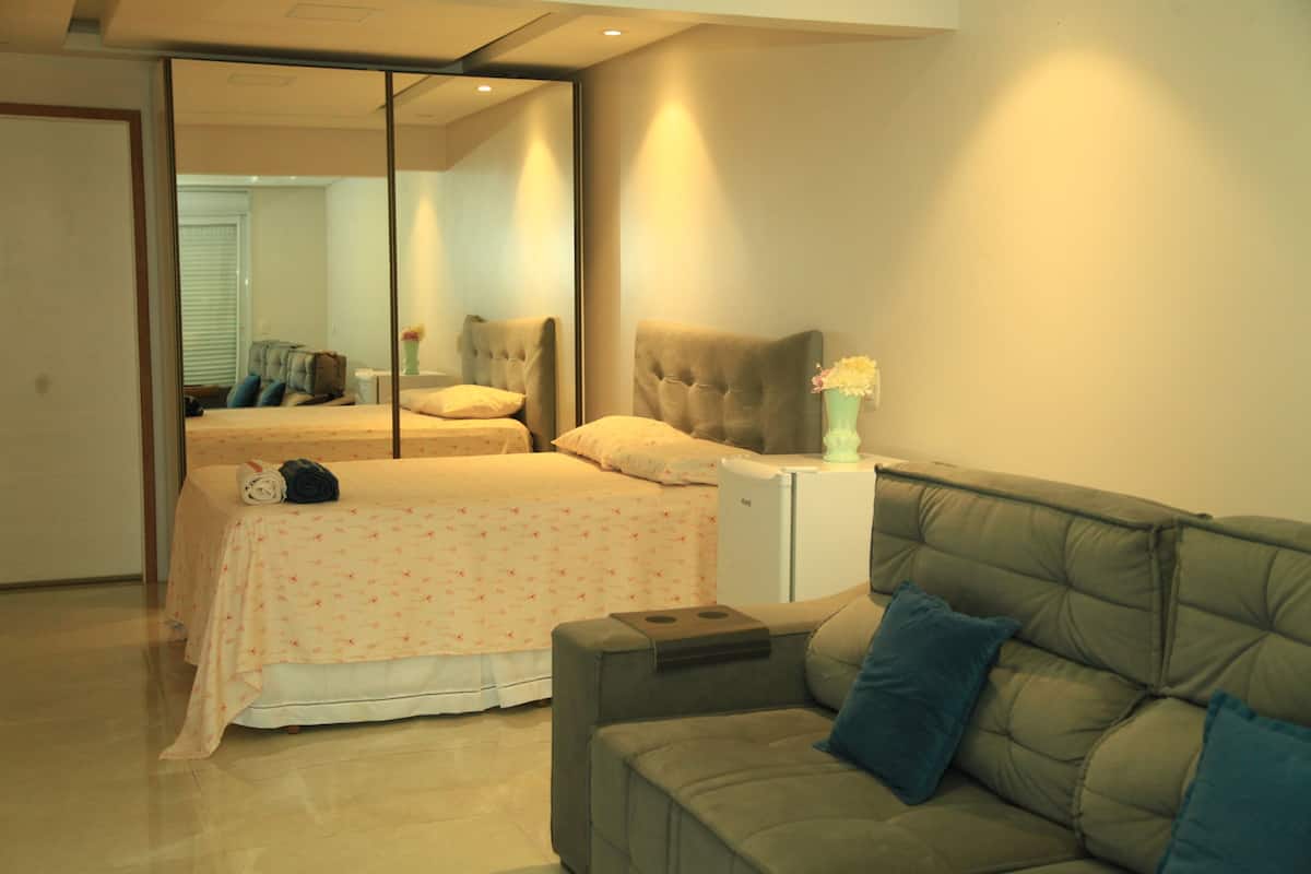 A bedroom with a bed, a sofa, a small table, and a mirror.