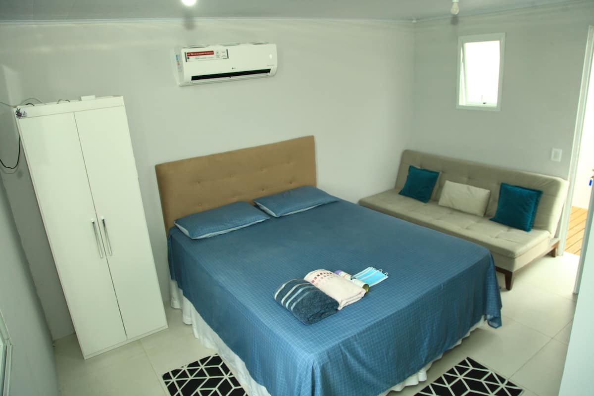 A bedroom with a bed, a sofa, a wardrobe, and an air conditioning unit.