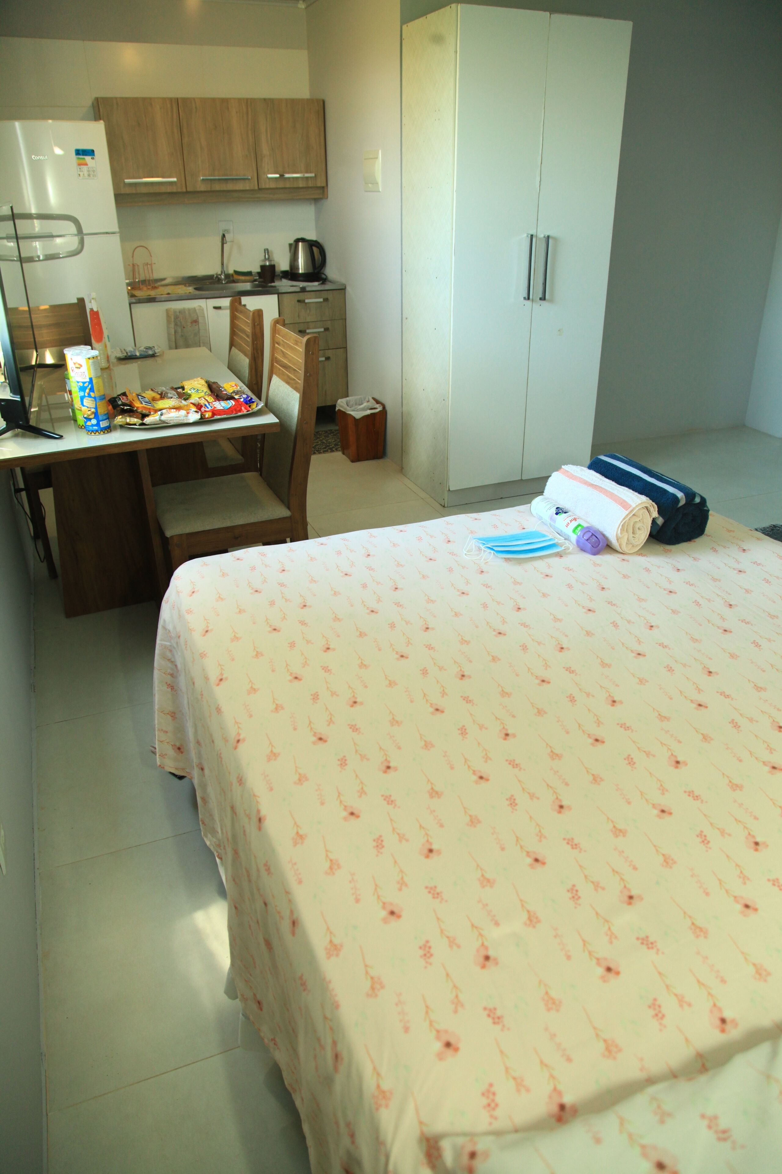Une chambre comprenant un lit, un bureau avec une chaise, une armoire et un coin cuisine.