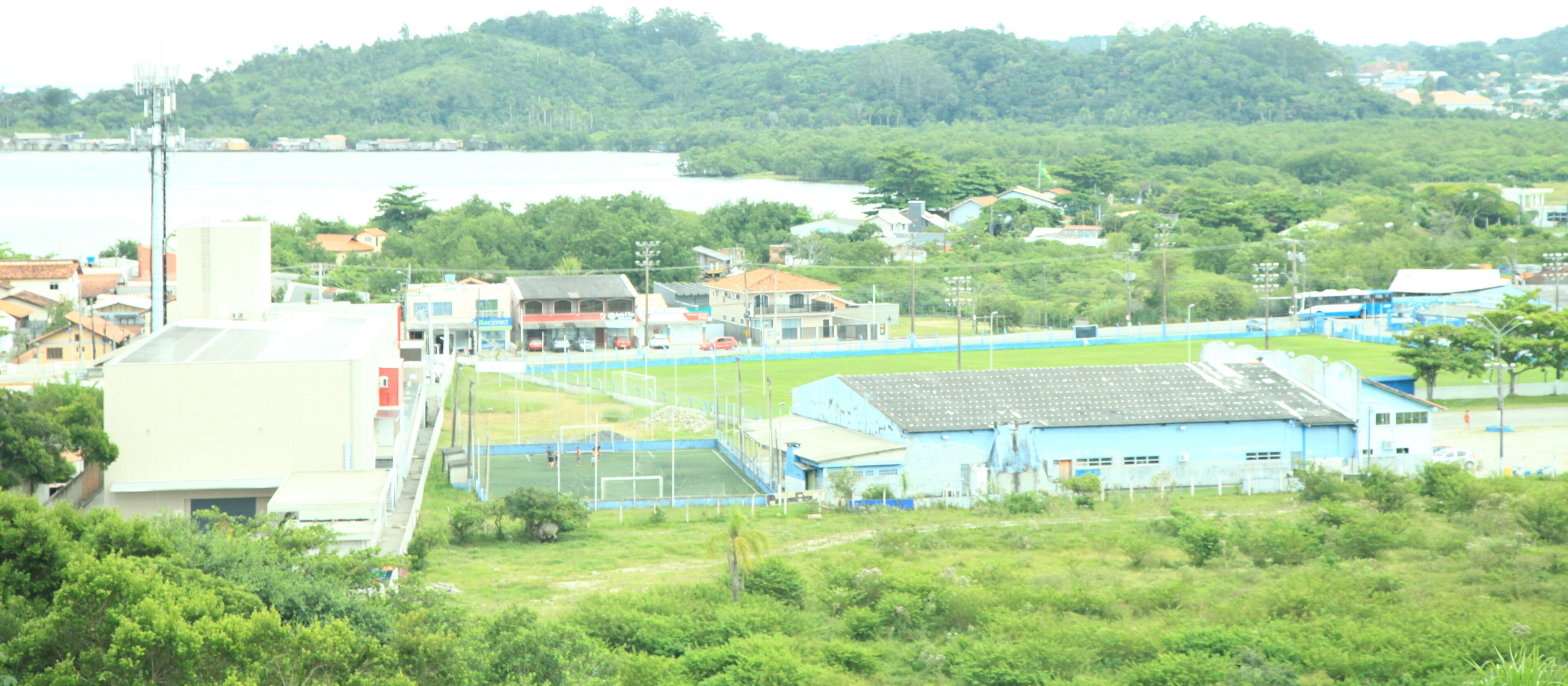 A residential area with houses, a soccer field, and a body of water in the background.