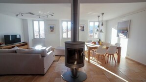 Un salon moderne doté d’un poêle à bois central, d’un canapé, d’une télévision et d’un coin repas avec des chaises et une table.