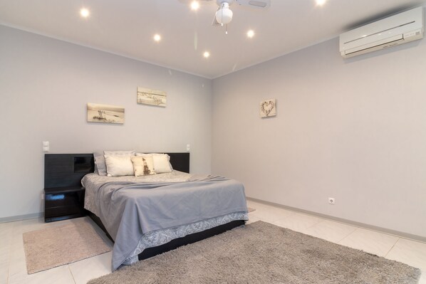 A modern bedroom with a large bed, a ceiling fan, recessed lighting, and an air conditioning unit.