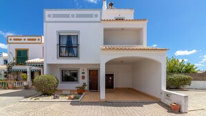 A modern two-story building with a tiled roof, a balcony, and a small garden area with potted plants. - Sunny family villa with pool, 10 mins from the beach and centre! (Ferragudo)