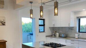 A modern kitchen with a large island, pendant lights, and a view of greenery outside. - Sunny family villa with pool, 10 mins from the beach and centre! (Ferragudo)