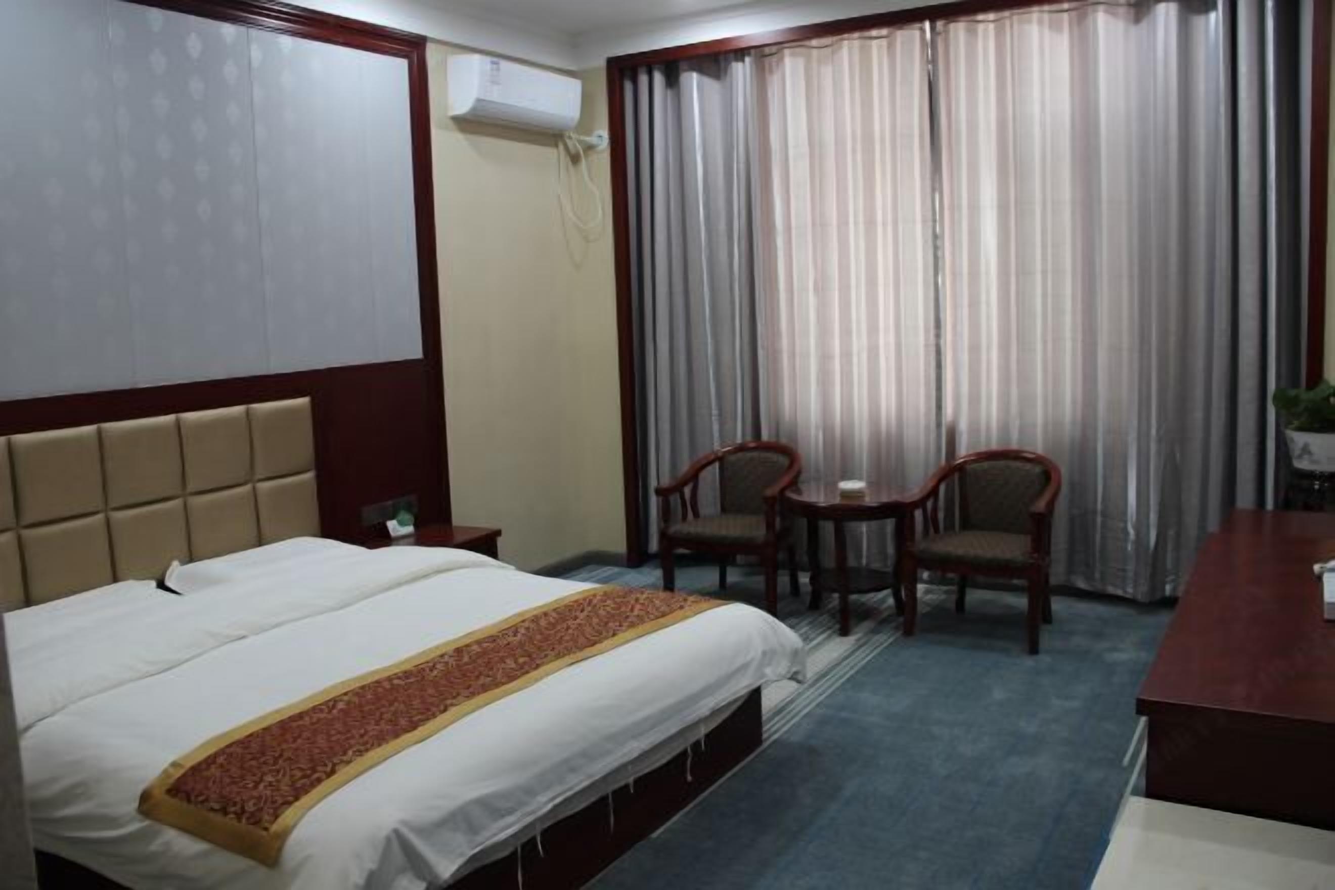 A hotel room with a bed, two chairs, a small table, and a desk.