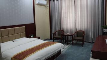 A hotel room with a bed, two chairs, a small table, and a desk.