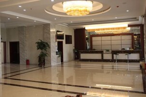 Un vestíbulo de hotel con una recepción, una lámpara de araña grande y un piso pulido.