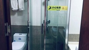 A small, enclosed shower area with a glass door, a toilet, and a caution wet floor sign. - Hengxiang Hotel (Aksay)