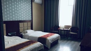A hotel room with two beds, a small table, a chair, and a window with curtains. - Hengxiang Hotel (Aksay)