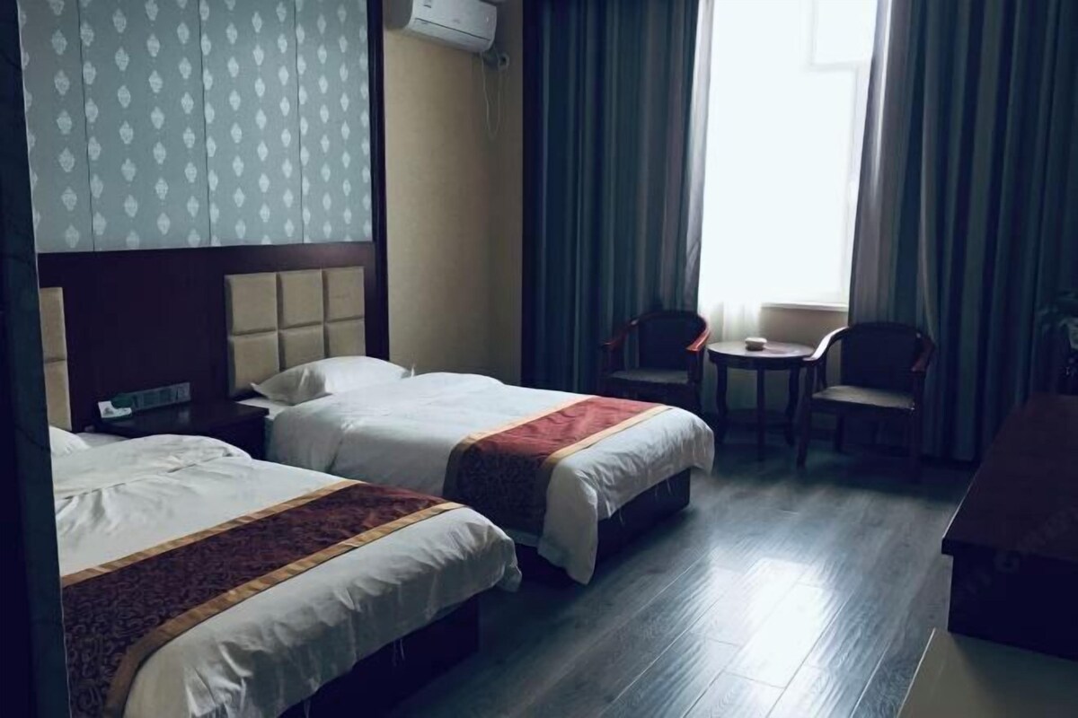 Habitación de hotel con dos camas, una mesita, una silla y una ventana con cortinas.