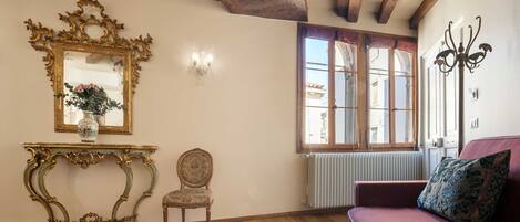 A room with a wooden ceiling, a large mirror, a sofa, a chair, and a small table with books.
