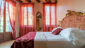 Une chambre avec un grand lit, des rideaux rouges, un miroir et une tête de lit à motifs floraux.