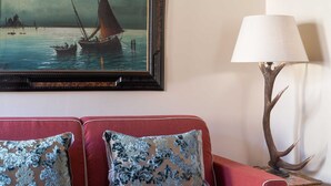 Un canapé rouge agrémenté de deux coussins décoratifs, un tableau encadré représentant un paysage marin et une lampe de table dont le pied est orné de motifs de bois de cerf.