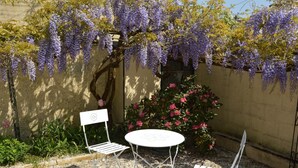 Un giardino con un tavolo e due sedie in metallo bianco, circondato da un vialetto sterrato e un muro.