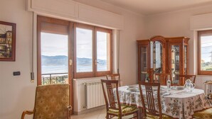 Ein Essbereich mit Tisch für vier Personen, Holzstühlen, einem Schrank mit Glastüren und Blick auf das Meer durch große Fenster.