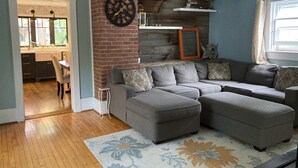 Ein Wohnzimmer mit einem Ecksofa, einer Zieruhr und einer Wand im Holzdesign.