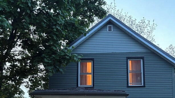 Ein zweistöckiges Haus mit Veranda, einer Holztür und einem Fenster mit dekorativem Glas.