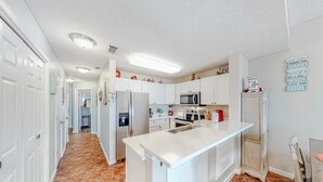 A modern kitchen with white cabinets, a central island, stainless steel appliances, and a tiled floor. - The Dunes 508 - Beach View & Bay View-Indoor-Outdoor Pool (Gulf Shores)