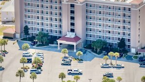 A multi-story hotel with a central courtyard, parking lot, and surrounding palm trees. - The Dunes 508 - Beach View & Bay View-Indoor-Outdoor Pool (Gulf Shores)