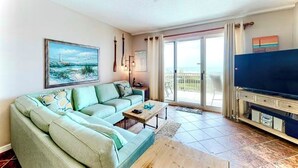 A living room with a sofa, a coffee table, a television, and a painting on the wall. - The Dunes 508 - Beach View & Bay View-Indoor-Outdoor Pool (Gulf Shores)