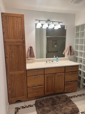 Un bagno con un mobile bagno in legno, un ampio specchio, un lavandino con dispenser di sapone e una zona doccia.