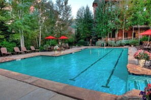 A swimming pool with lounge chairs and umbrellas, surrounded by trees and a building.