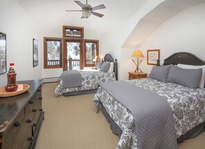 A bedroom with two beds, a ceiling fan, a dresser, a lamp, and a window with a view of trees. - Charlie's Slopeside: Ski-In/Out, Sleeps 10, 2 Master Suites, Pool + Hot Tub, Alpine Club (Avon)