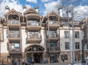 A multi-story building with balconies, a stone facade, and a large entrance.