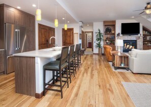 A modern kitchen with a central island, bar stools, wooden cabinets, and a built-in refrigerator. - Charlie's Slopeside: Ski-In/Out, Sleeps 10, 2 Master Suites, Pool + Hot Tub, Alpine Club (Avon)