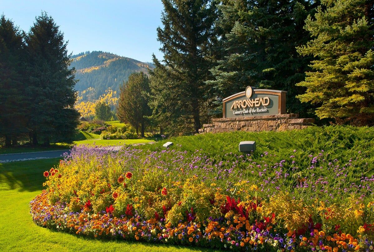 A sign for Arrowhead Country Club of the Rockies with a landscaped garden in the foreground.