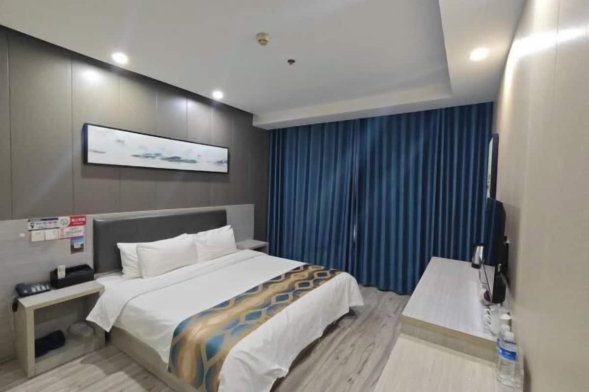 A hotel room with a bed, bedside table, and a desk with a chair.