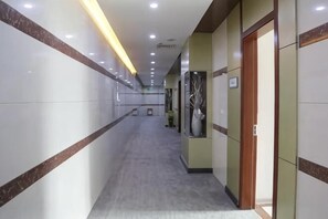 A hotel corridor with a marble floor, wooden doors, and recessed lighting. - Jinzhu Business Hotel (Xiangshui)