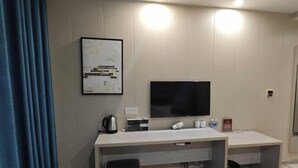 Una habitación de hotel moderna con una televisión de pantalla plana grande, un escritorio con una silla, una cafetera y un cuadro en la pared.