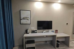 Une chambre d’hôtel moderne équipée d’un grand téléviseur à écran plat, d’un bureau avec une chaise, d’une machine à café et d’un tableau encadré au mur.