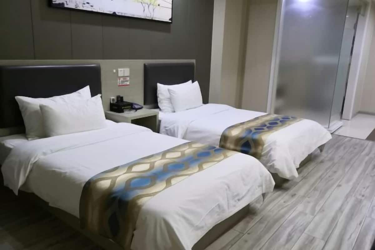 A hotel room with two beds, a nightstand, a wall-mounted artwork, and a sliding door.